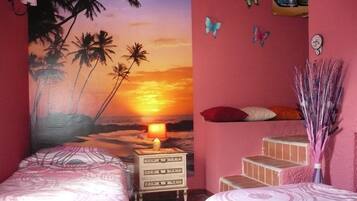 Quarto com duas camas, uma mesinha de cabeceira, um mural na parede com pôr do sol e um pequeno lance de escadas.