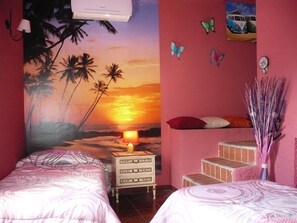 Un dormitorio con dos camas, una mesita de noche, un mural en la pared con un atardecer y una pequeña escalera.