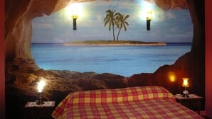 A bedroom with a bed, a nightstand, and a wall mural of a beach scene with palm trees and a sunset. - chalet bougainvillea sea view 500 m. from the beach available wifi (Almuñécar)