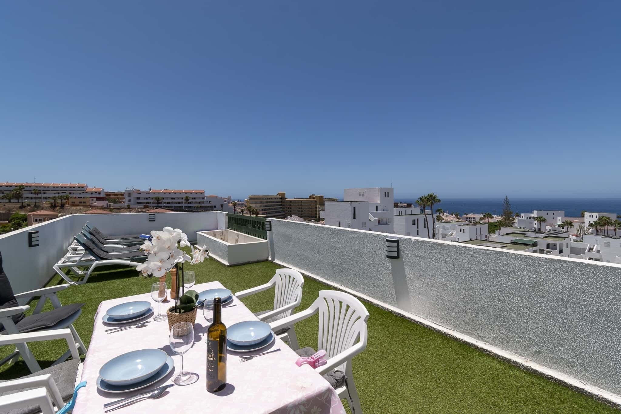 A rooftop terrace with a table set for dining, overlooking a coastal cityscape.