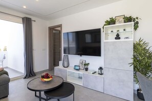 Ein modernes Wohnzimmer mit Flachbildfernseher, Glastisch mit Früchten, einer Couch und einer Topfpflanze.