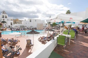 A poolside area with lounge chairs, umbrellas, and a dining area with tables and chairs.