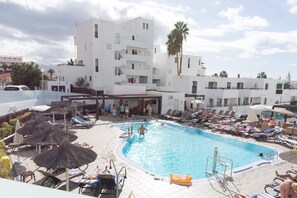 A swimming pool with lounge chairs and umbrellas, surrounded by white buildings with balconies. - Sunset Bay 45 - Two Bed (Costa Adeje)