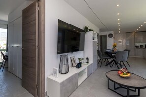 Ein modernes Wohnzimmer mit Flachbildfernseher, Essbereich mit Tisch und Stühlen sowie Küchenzeile mit Schränken und Geräten.