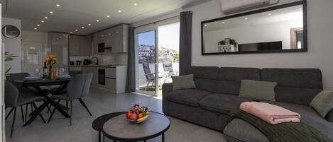 A modern apartment with a dining area, a living room with a sofa and a coffee table, and a kitchen with a view.