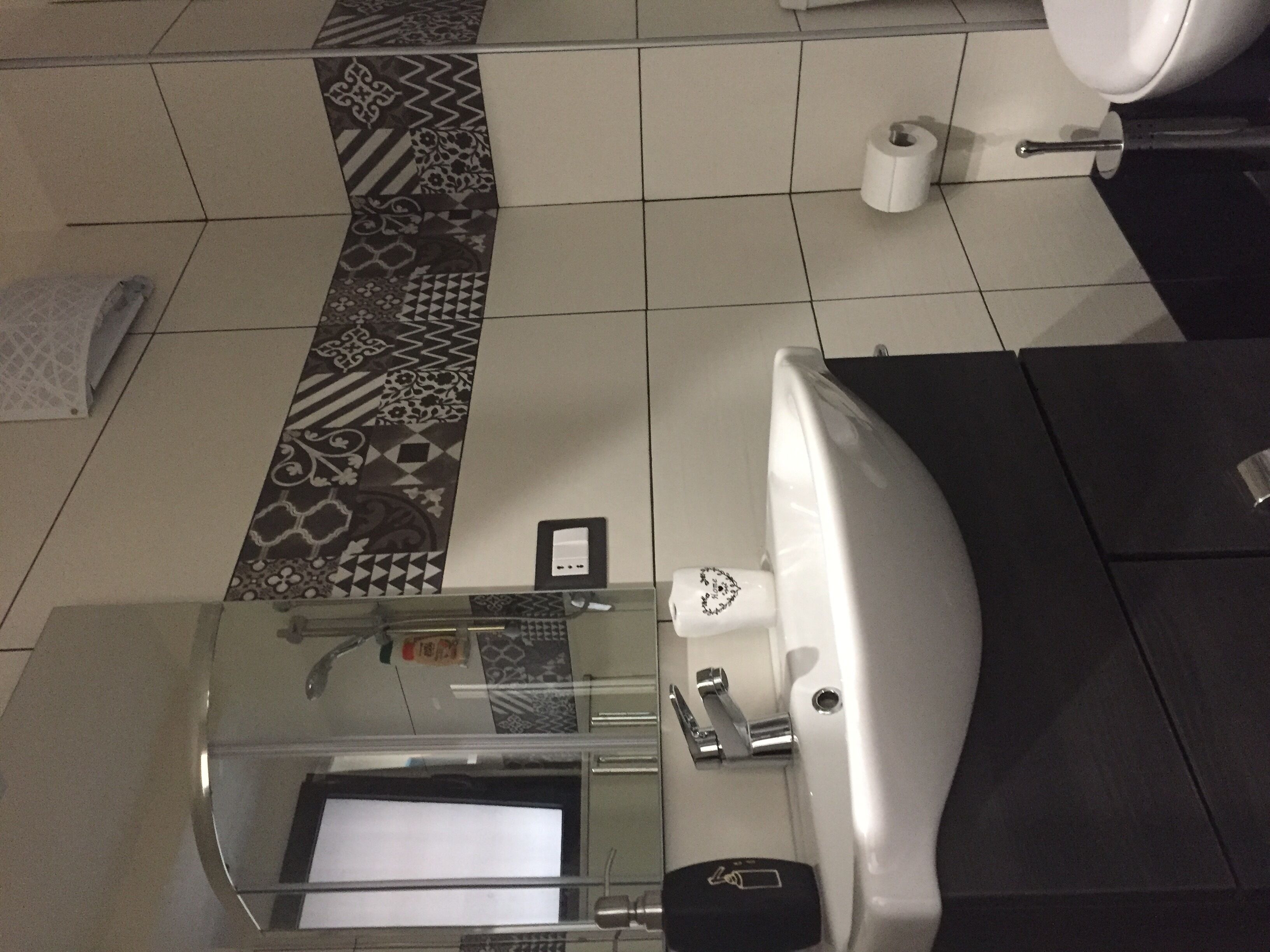 A bathroom with a white sink, a glass shower enclosure, a patterned floor, and a toilet.