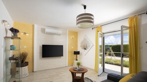 Una sala de estar moderna con un televisor de pantalla plana, un sofá, una mesita redonda y un aparador de vidrio.