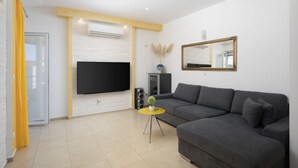 Un salón moderno con un sofá gris, una mesa de centro amarilla, un televisor de pantalla plana y un espejo grande en la pared.