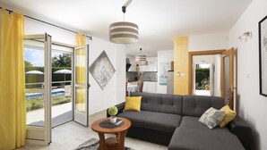 Una sala de estar moderna con un sofá gris, cojines amarillos, una pequeña mesa redonda con una planta y un amplio ventanal con cortinas amarillas.