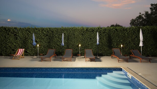 Piscina con sillones de descanso y sombrillas, rodeada por un seto.