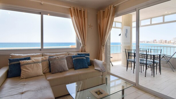 Ein modernes Wohnzimmer mit einem beigen Sofa, einem Glastisch und Meerblick durch große Fenster.