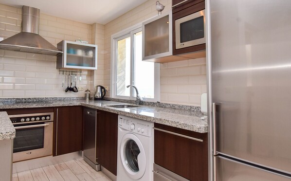 A modern kitchen with stainless steel appliances, a built-in oven, a dishwasher, and a washing machine.