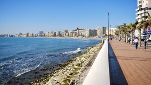 Eine Küstenpromenade mit Steinweg, Strand und Gebäuden im Hintergrund.