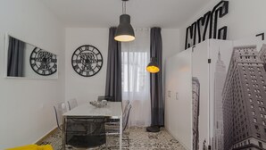 A dining area with a white table, clear chairs, black pendant lights, and a yellow sofa.