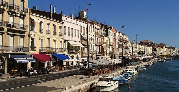 Une rue bordée de bâtiments, avec des terrasses et des bateaux amarrés le long du quai.