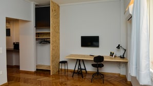 A modern, compact living space with a wooden dining table, two black chairs, a mounted TV, and a ceiling light fixture.