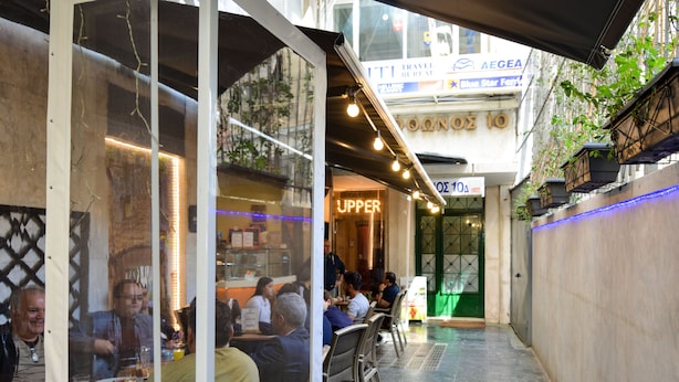 An outdoor dining area with tables and chairs, a glass partition, and a sign for 'UPPER'.