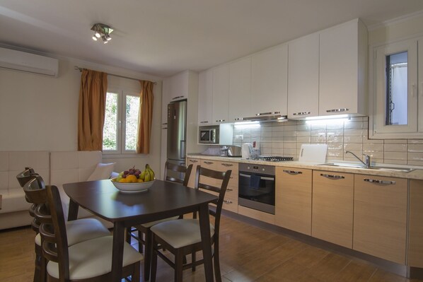 Una cocina moderna con armarios blancos, una mesa de comedor con sillas, un frutero y una ventana con cortinas.