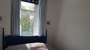 Een slaapkamer met een bed, een raam met gordijnen en een wandlamp.
