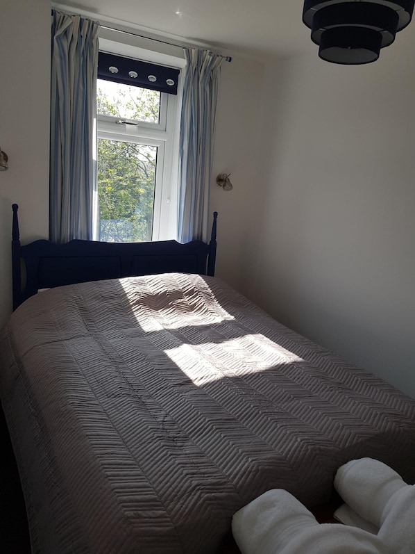 Une chambre à coucher avec un lit, une fenêtre avec des rideaux et un luminaire fixé au mur.