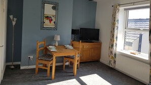 Een kamer met een houten tafel en stoelen, een televisie, een spiegel en een raam met uitzicht op zonnepanelen.
