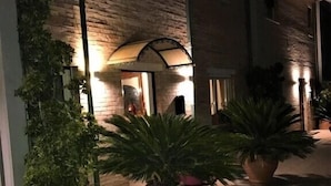Un bâtiment à la façade en briques et à l’entrée carrelée. De grands pots de plantes sont placés au premier plan.