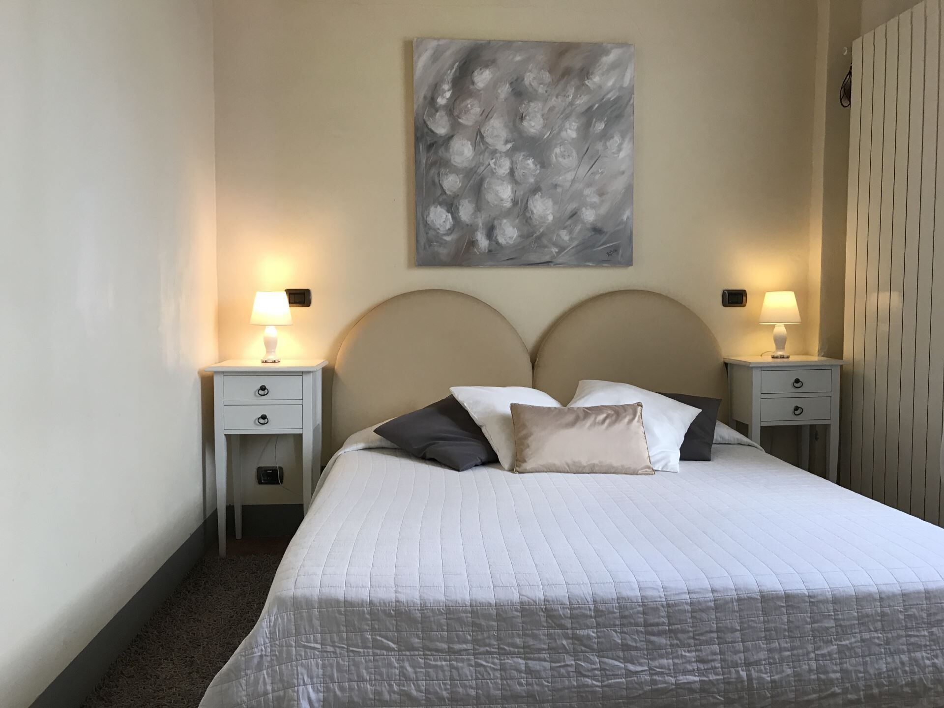 Un letto rifatto con copriletto trapuntato, due comodini con lampade e un grande quadro astratto appeso al muro.