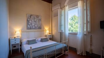 A bedroom with a bed, bedside lamps, a painting, a window with curtains, and a radiator.