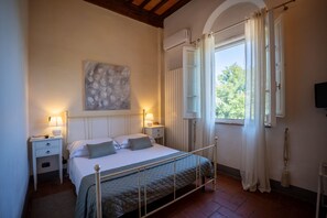 Ein Schlafzimmer mit Bett, Nachttischlampen, einem Gemälde, einem Fenster mit Vorhängen und einer Heizung.