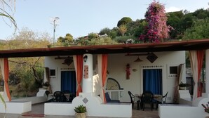 A covered outdoor seating area with tables and chairs, a potted plant, and a view of the surrounding landscape. - Holiday home Kristin (Lipari)