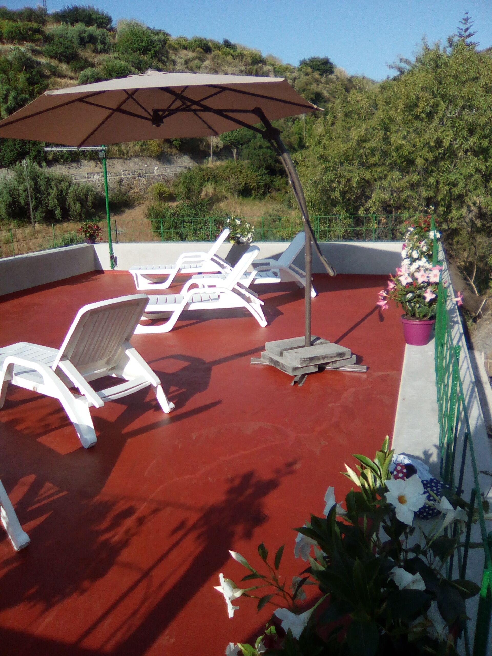 A red-tiled outdoor area with white lounge chairs and a large umbrella.