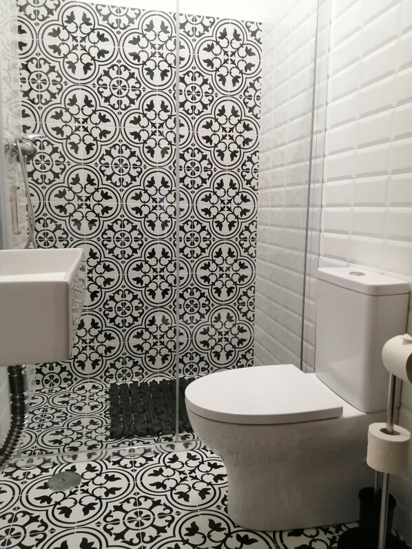 A bathroom with black and white patterned tiles, a white sink, a toilet, and a shower area.