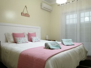 A neatly made bed with pink and floral pillows, a pink bedspread, and two folded towels.