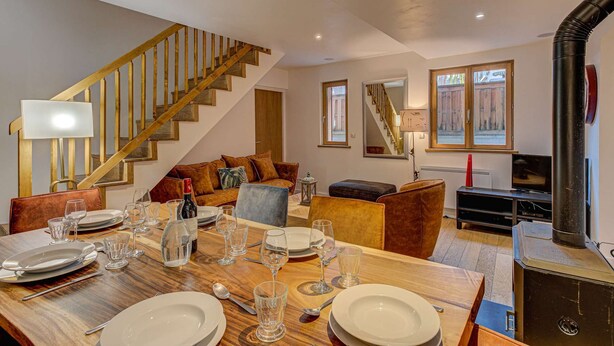 A dining area with a wooden table set for six, a sofa, and a staircase.