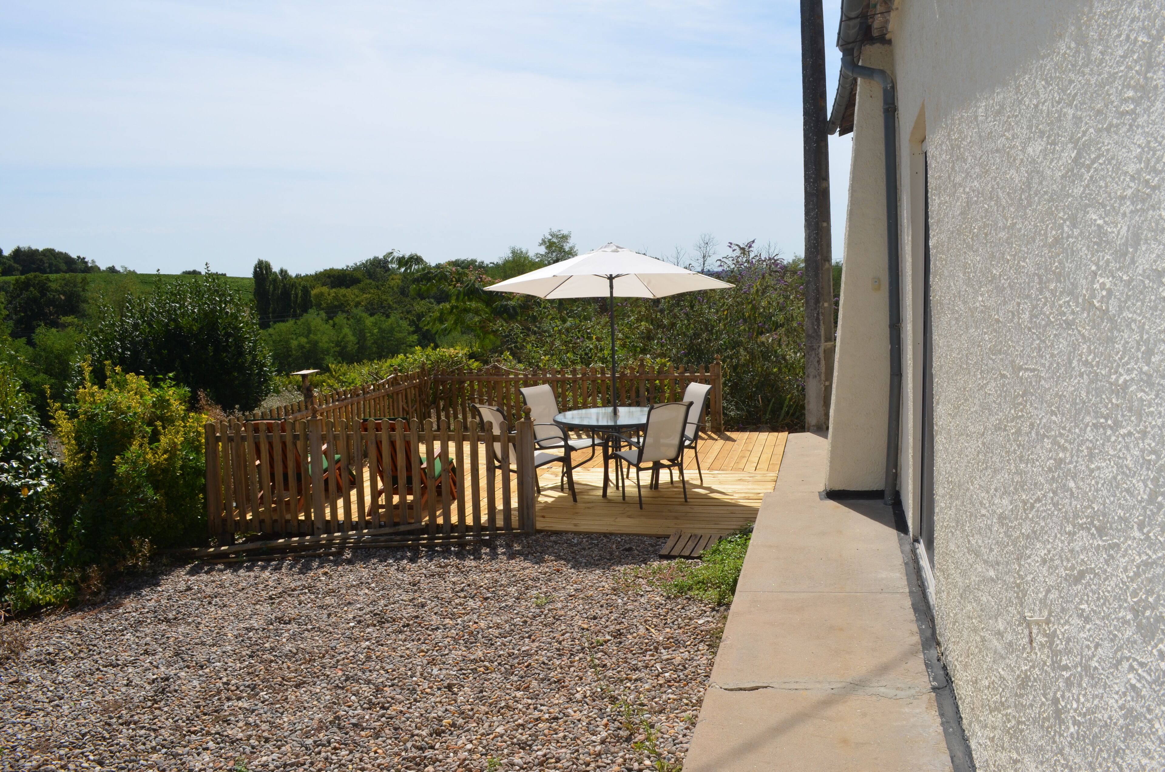 Una terrazza esterna con tavolo e sedie, un ombrellone e un recinto in legno.
