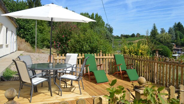 A wooden deck with a glass table and chairs, a white umbrella, and a wooden fence. - The Cottage  near Sainte Foy la Grande (Fougueyrolles)