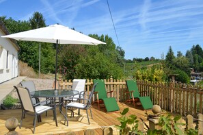 Eine Holzterrasse mit einem Glastisch und Stühlen, einem weißen Sonnenschirm und einem Holzzaun.