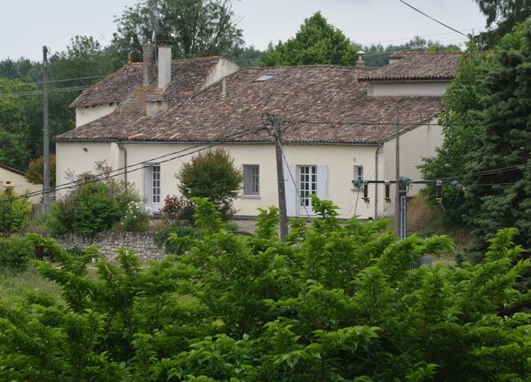 Ein traditionelles Haus mit Ziegeldach, Steinmauer und üppiger Bepflanzung im Vordergrund.