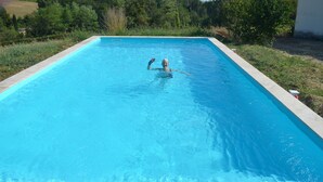 A rectangular swimming pool with clear blue water, surrounded by greenery and a white building in the background. - The Cottage  near Sainte Foy la Grande (Fougueyrolles)