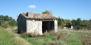 Ein kleines Steinhaus mit einem Ziegeldach, umgeben von Gras und Bäumen.