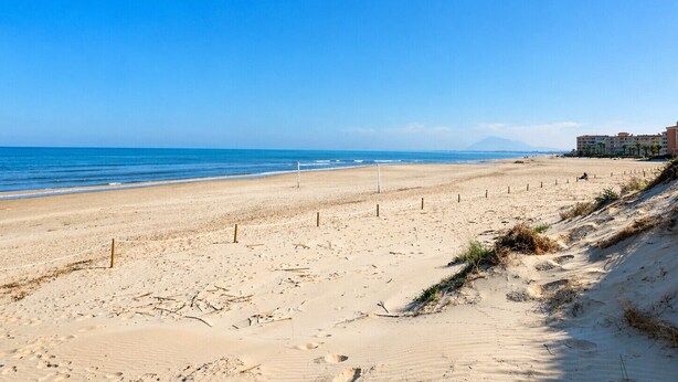 A beach with a clear sky, a sandy shore, and a building in the background.