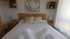 A neatly made bed with two rolled towels, a wooden headboard, and two nightstands with lamps.