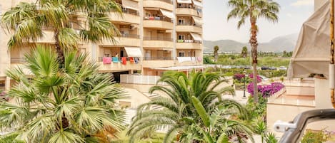 A multi-story hotel with balconies, palm trees, and a view of mountains.