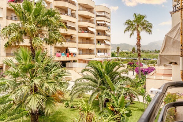 A multi-story hotel with balconies, palm trees, and a view of mountains.
