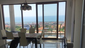 Un comedor con una mesa y sillas, un ventilador y vista al mar a través de amplios ventanales.
