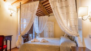 A bedroom with a four-poster bed, a wooden ceiling, and a red chair.