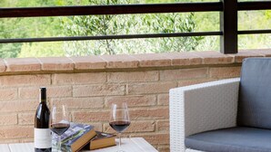 A balcony with a view of a historic building, a table with a wine bottle and glasses, and a wicker chair.