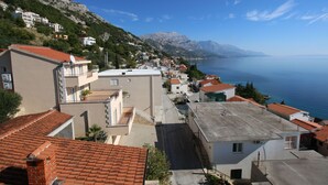Un poble costaner amb edificis al llarg d'un carrer, vista clara del mar i muntanyes al fons.