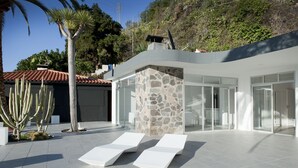 Ein moderner Außenbereich mit einer Steinmauer, Glastüren und weißen Loungestühlen.