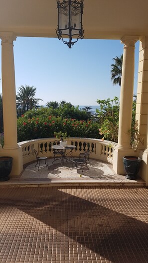 A covered patio with a round table and chairs, surrounded by a low wall with potted plants and a view of the sea. - Idyllic flat Cannes, sea view, 1. 200km Croisette, very calm (Cannes)